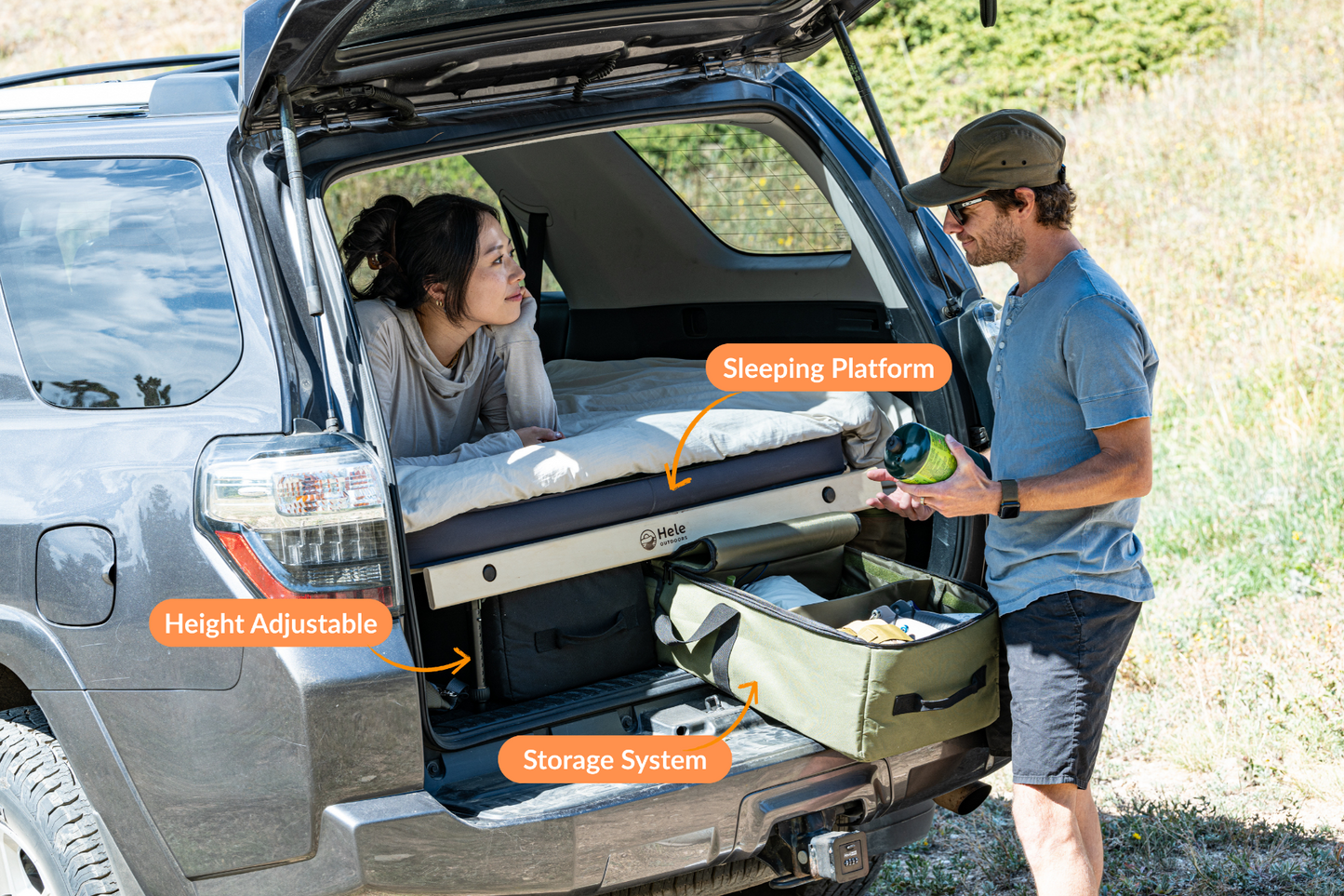 Two people interacting with a sleeping platform in the back of a vehicle, with labels indicating height adjustable and storage system features.