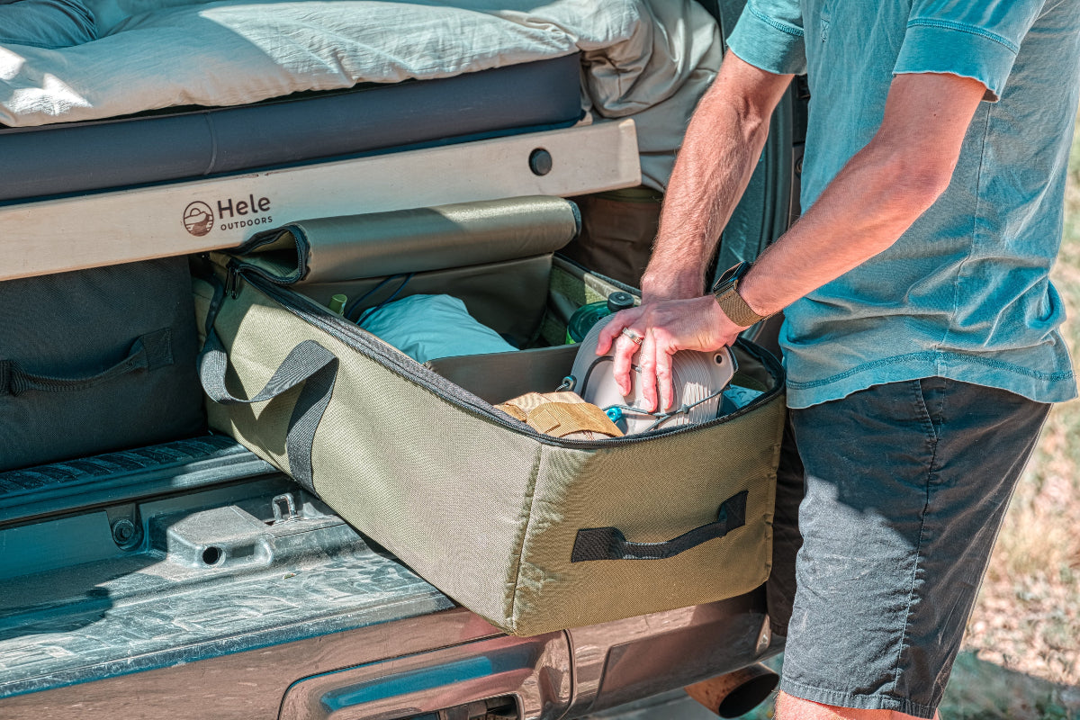 Person organizing items in a camping storage bin attached to a vehicle.